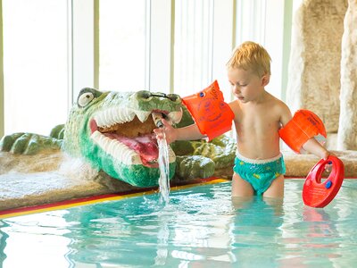 Kleiner Junge spielt mit Krokodilfigur im Wasser