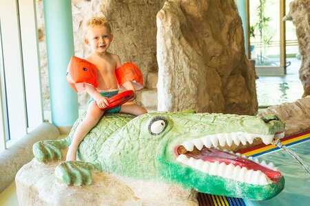 Kind sitzt auf Krokodil im Hallenbad