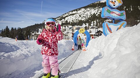 Kind fährt auf Zauberteppich beim Skikurs